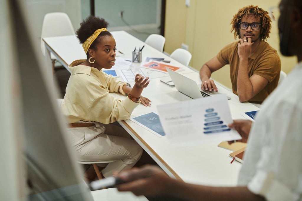 Colleagues discuss printed charts around a meeting table with a laptop.